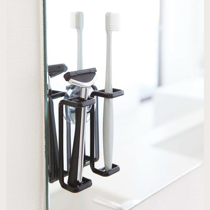Black Toothbrush Holder holding toothbrush and razor on bathroom mirror by Yamazaki Home.