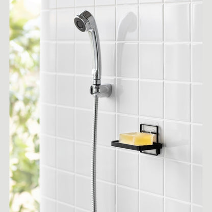 Yamazaki Home's black Traceless Adhesive Soap Tray in a shower, holding a bar of soap next to a silver shower hose on tiled wall.