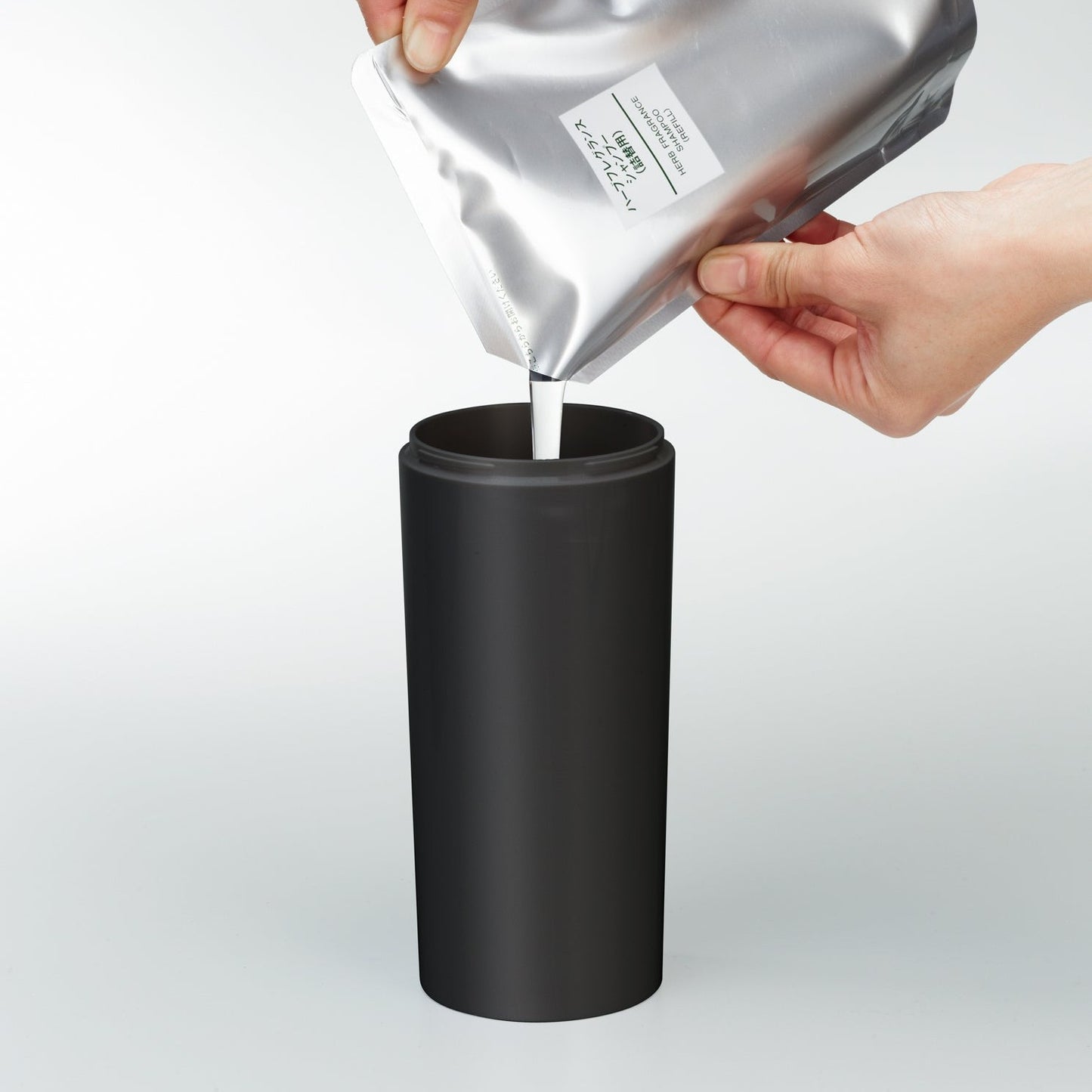 Front view of black Shampoo Dispenser getting filled with shampoo on white background by Yamazaki Home.