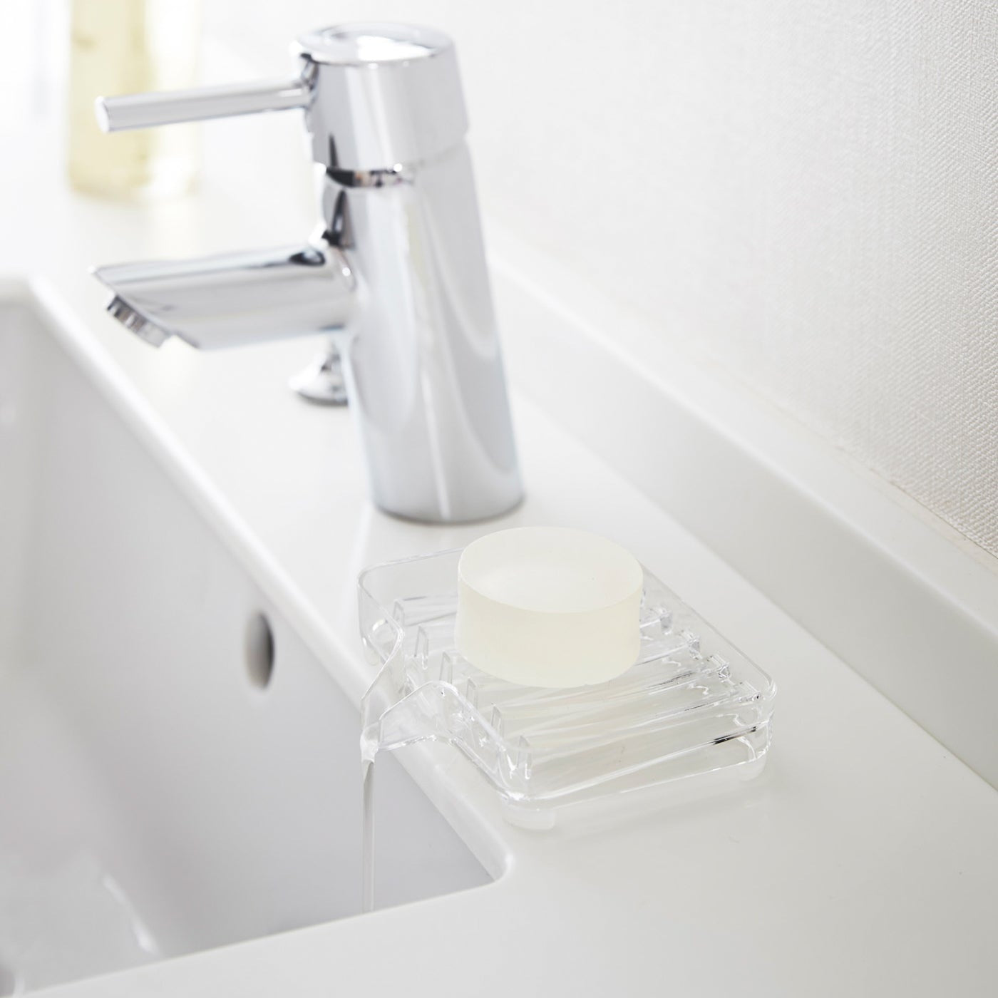 Clear Self-Draining Soap Tray holding soap on sink counter by Yamazaki Home.