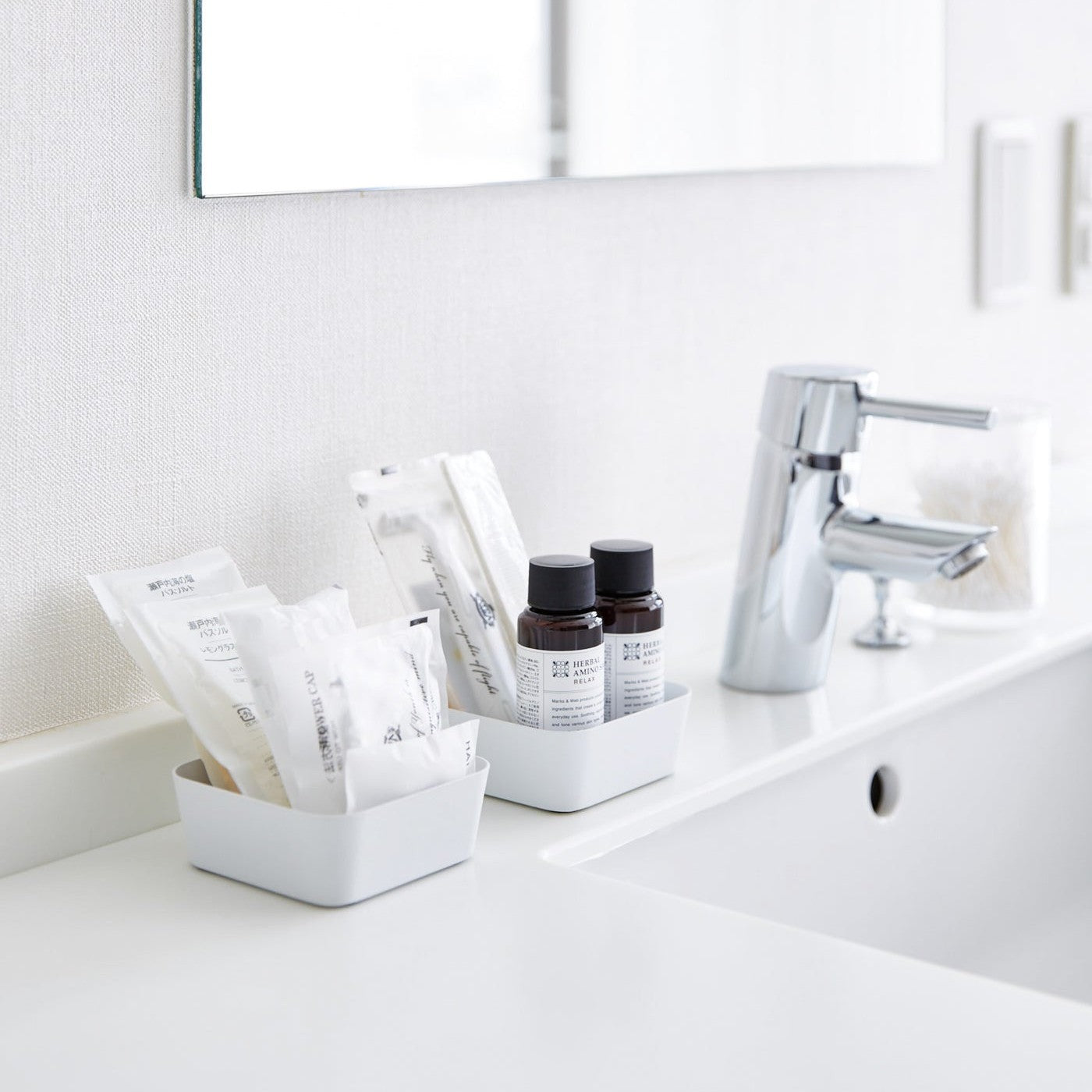 Small white Accessory Trays holding beauty products on bathroom sink counter by Yamazaki Home.