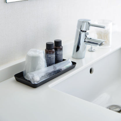 Flat black Accessory Tray holding toothbrush, cup, and soap on bathroom sink counter.