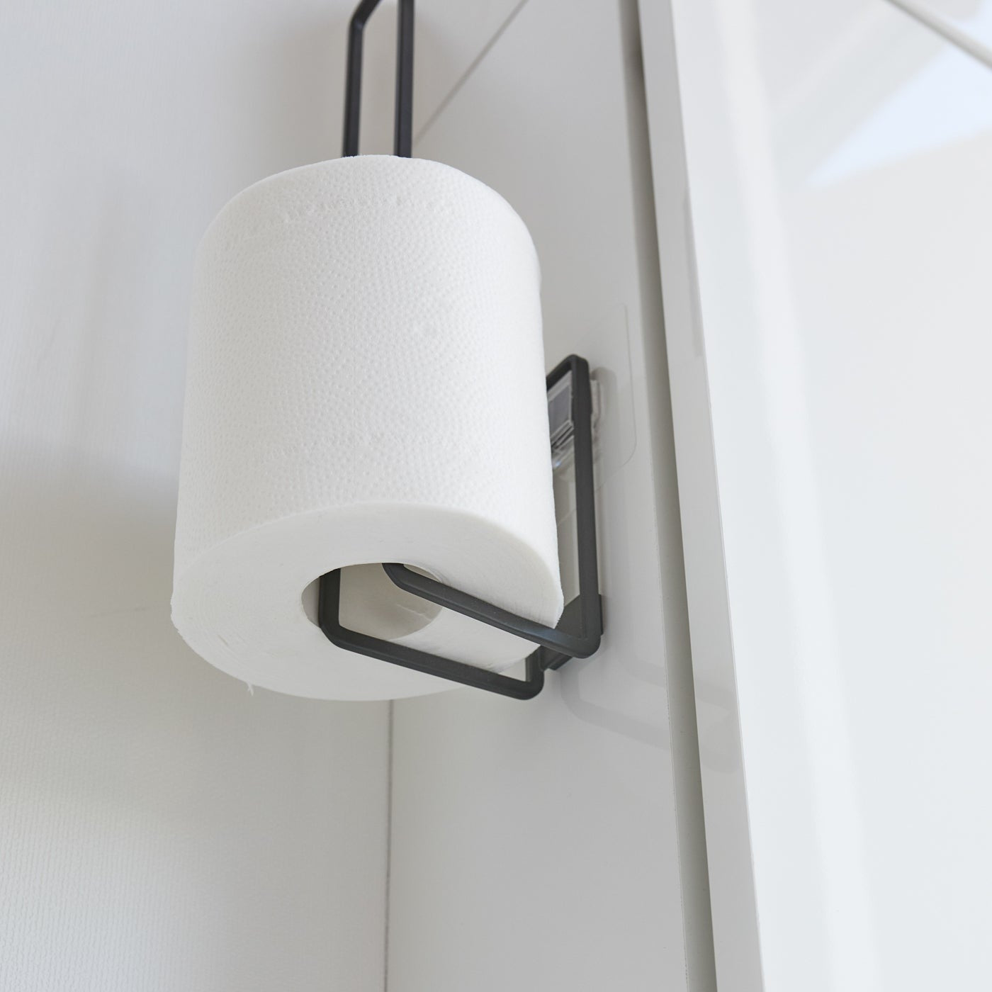 Close up of underside of black Yamazaki Home Traceless Adhesive Toilet Paper Holder with a roll stored