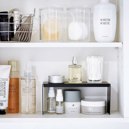 Open medicine cabinet showing black countertop riser on bottom shelf. Upper level of the riser holds perfume and hair products, while skincare and small sprays are stored on the bottom.