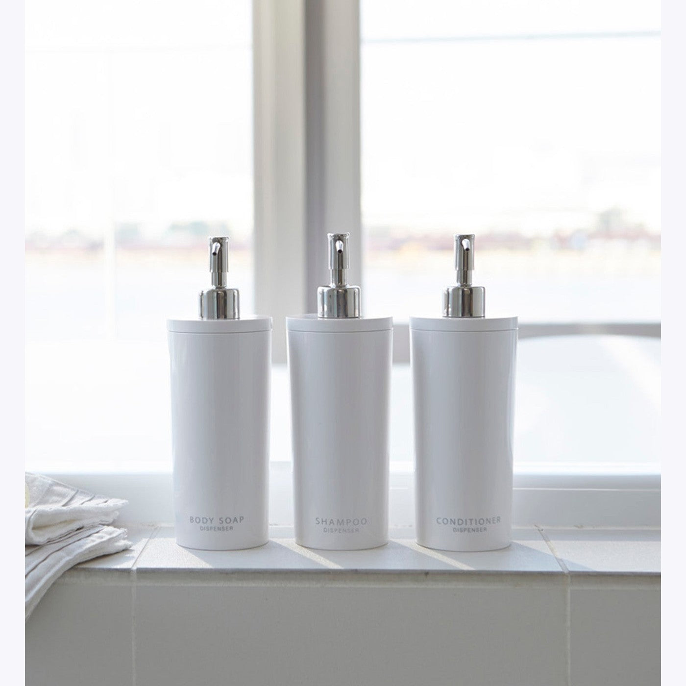 Front view of Yamazaki Home white Shampoo, Conditioner, and Body Soap dispensers in bathroom.