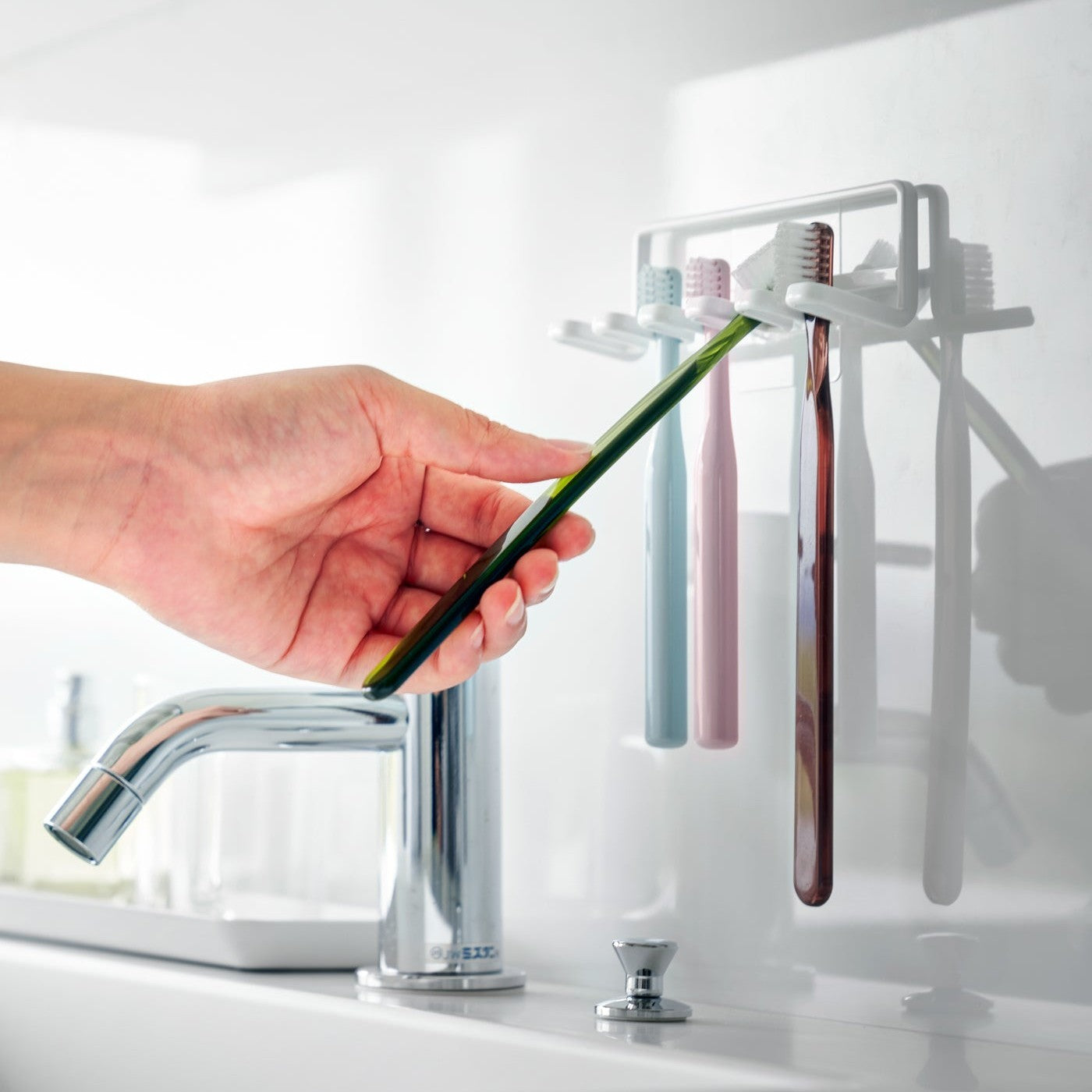 Yamazaki Home's Traceless Adhesive Toothbrush Holder, white, mounted on a bathroom wall with four colorful toothbrushes and a chrome faucet.