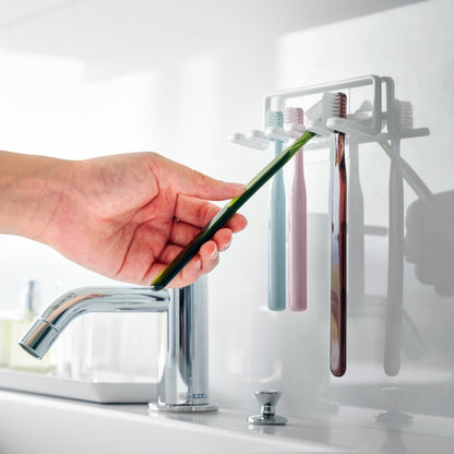 Yamazaki Home's Traceless Adhesive Toothbrush Holder, white, mounted on a bathroom wall with four colorful toothbrushes and a chrome faucet.