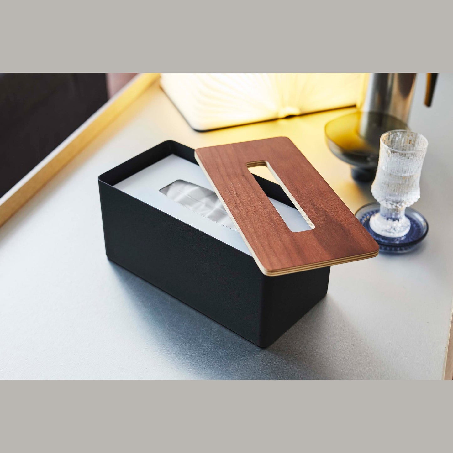 Yamazaki Home black Tissue Case with cover removed holding tissues on coffee table.