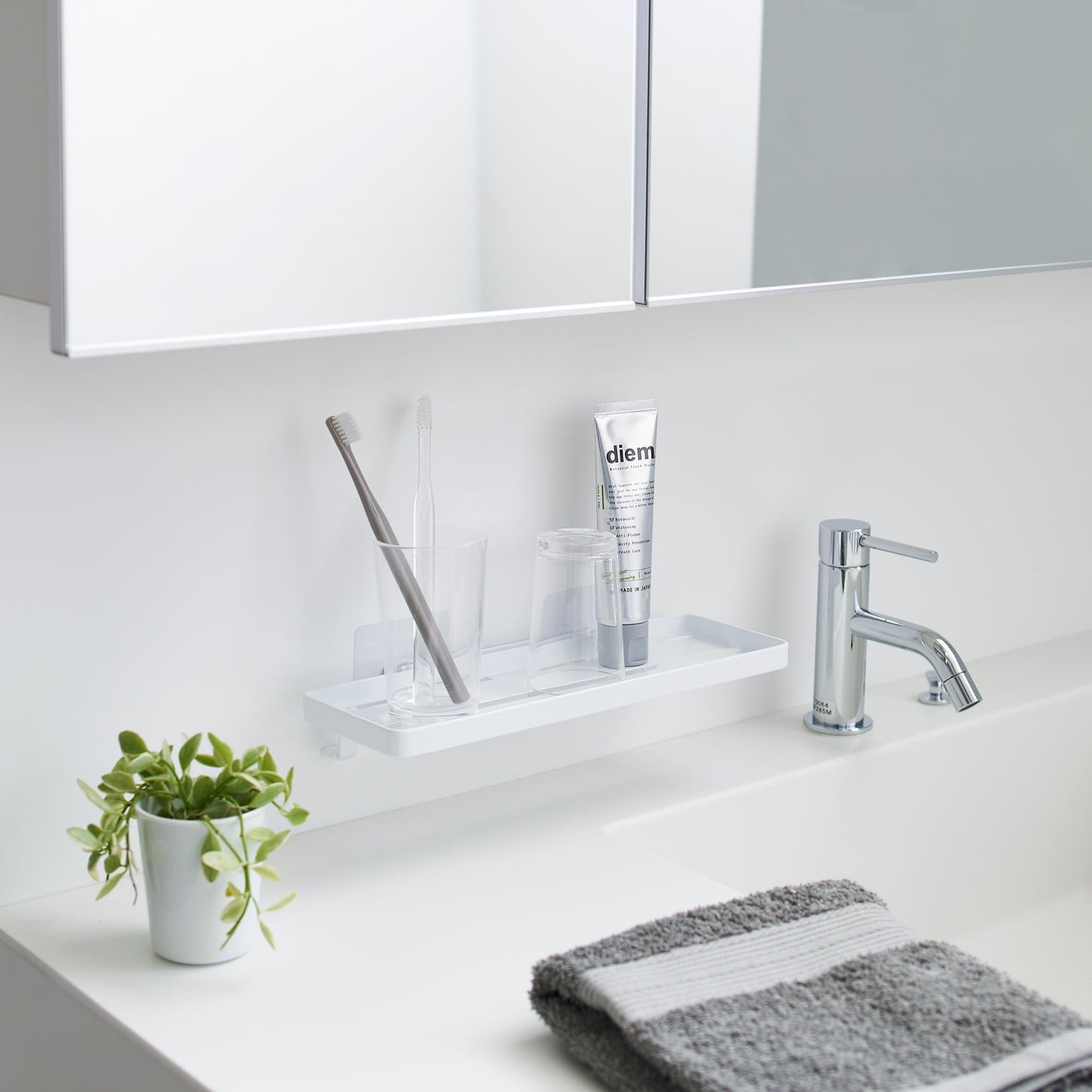Yamazaki Home Traceless Adhesive Floating Tray with a glass and toothbrush resting on it