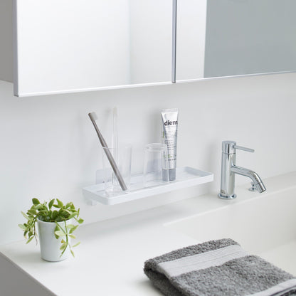 Yamazaki Home Traceless Adhesive Floating Tray with a glass and toothbrush resting on it
