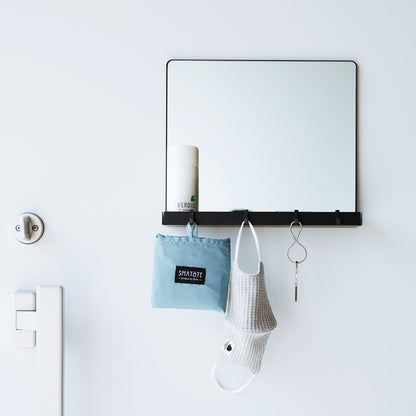 A black Yamazaki Magnetic Mirror With Storage Rack attached to a door holding bottles.