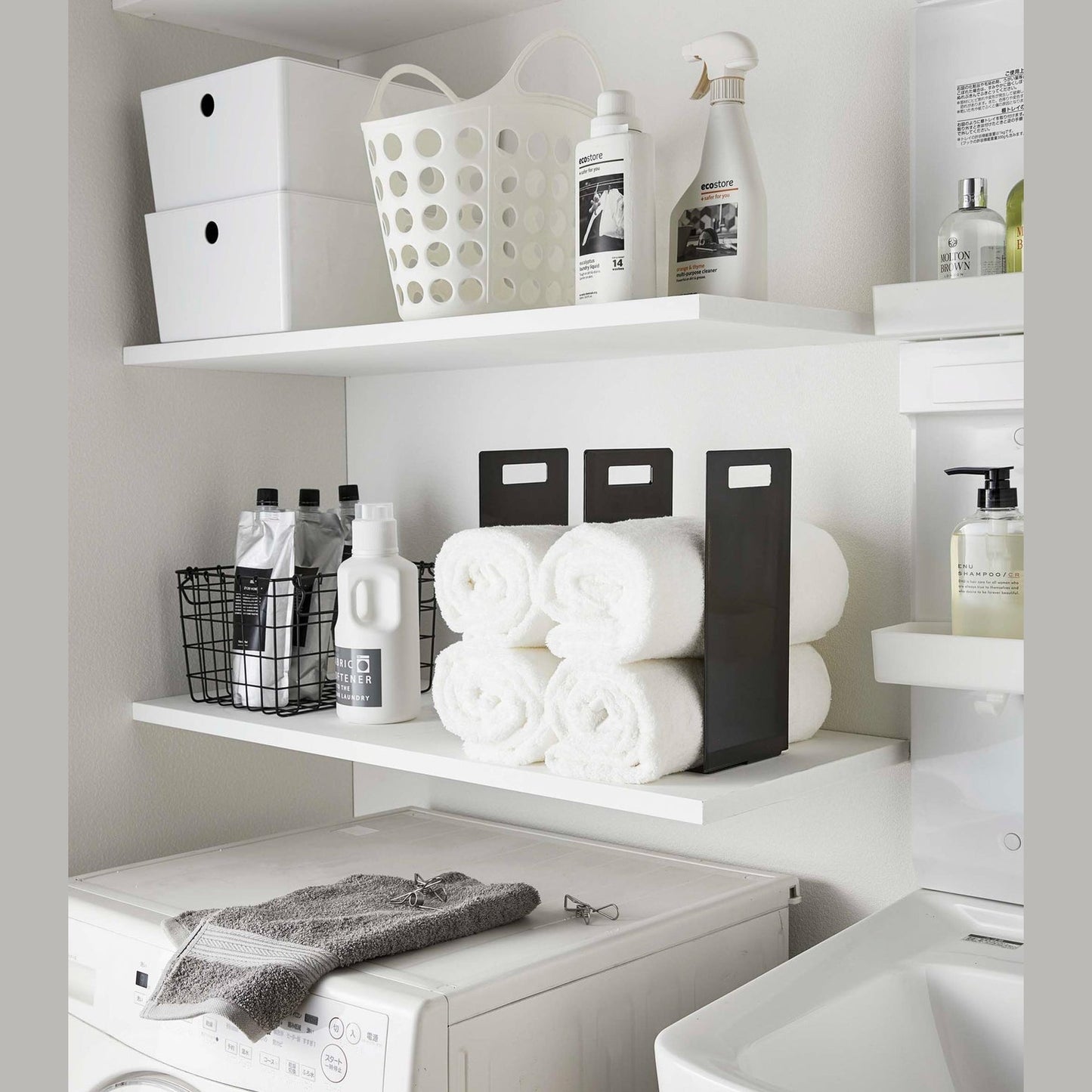 Black Towel Storage Organizer holding towels on laundry room shelf by Yamazaki Home.