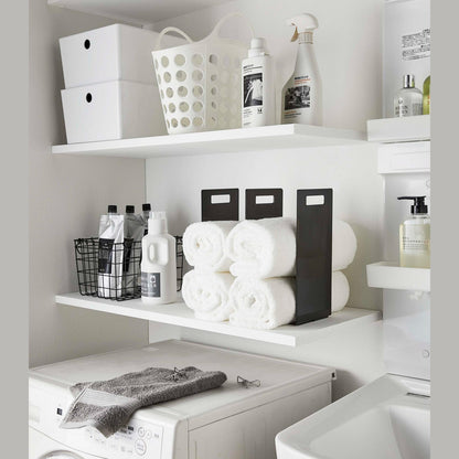 Black Towel Storage Organizer holding towels on laundry room shelf by Yamazaki Home.