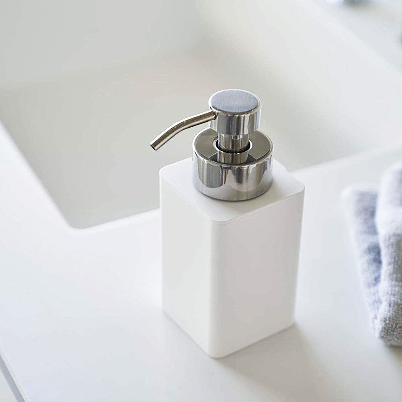 Close up view of white Foaming Soap Dispenser on sink counter by Yamazaki Home.