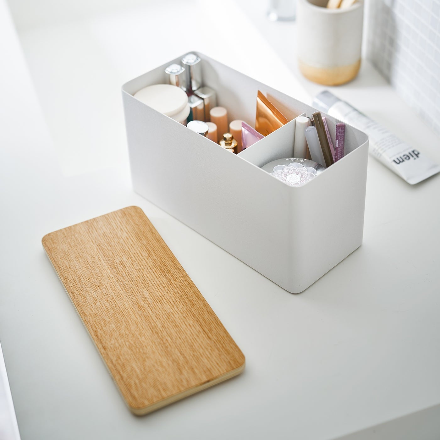 White Countertop Organizer holding makeup products with cover off on bathroom countertop by Yamazaki Home.