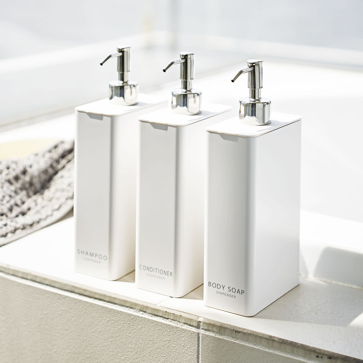 Yamazaki Home white Shampoo, Conditioner, and Body Soap dispensers next to the bathtub.