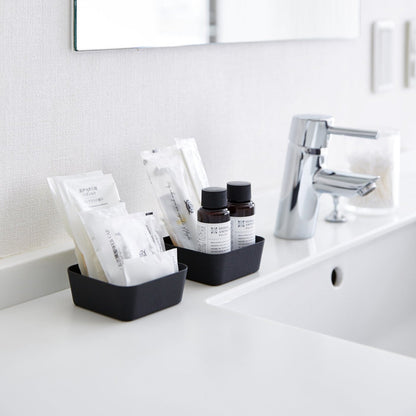 Small black Accessory Trays holding beauty items on bathroom sink counter by Yamazaki Home.