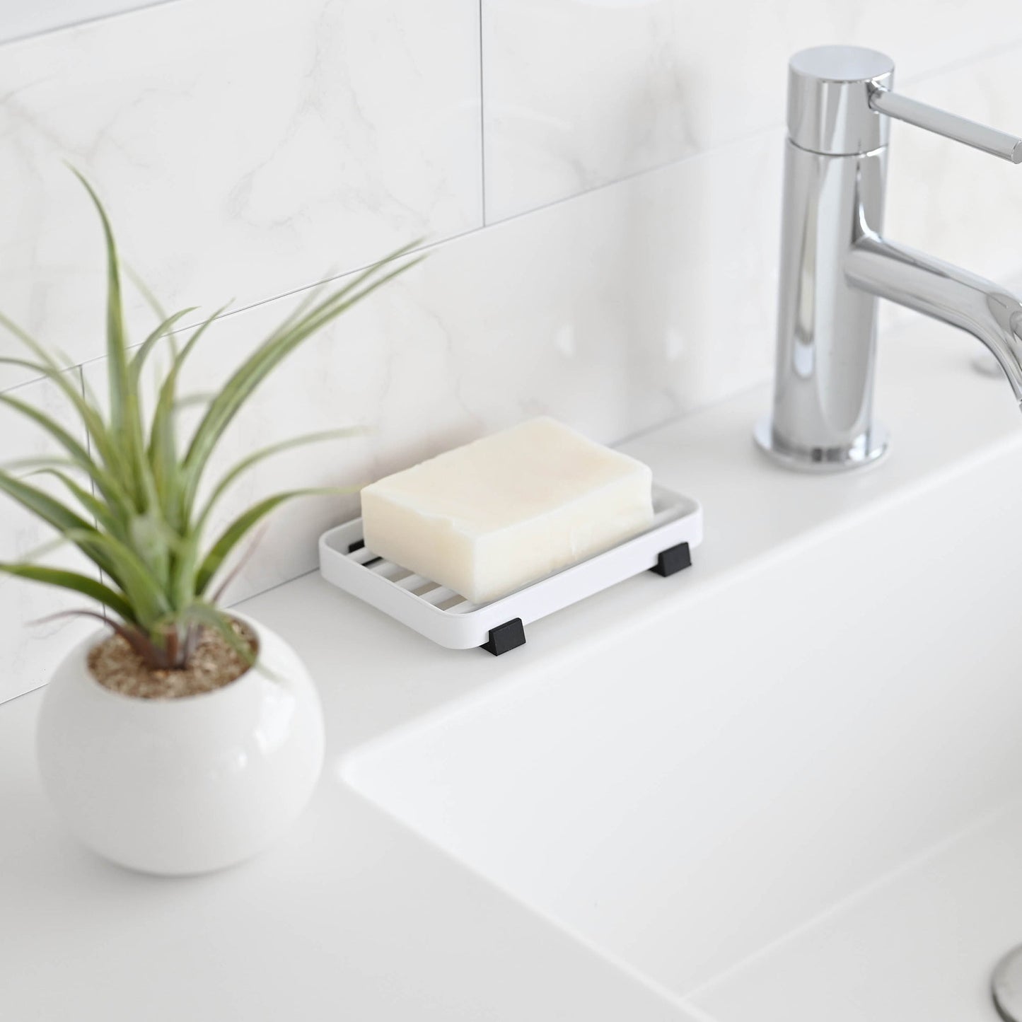 Side view of White Slotted Soap Tray holding soap bar on bathroom countertop by Yamazaki Home.