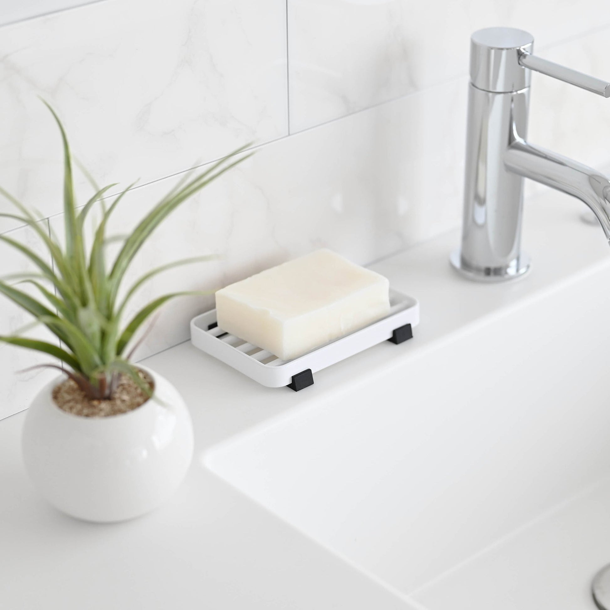 Side view of White Slotted Soap Tray holding soap bar on bathroom countertop by Yamazaki Home.