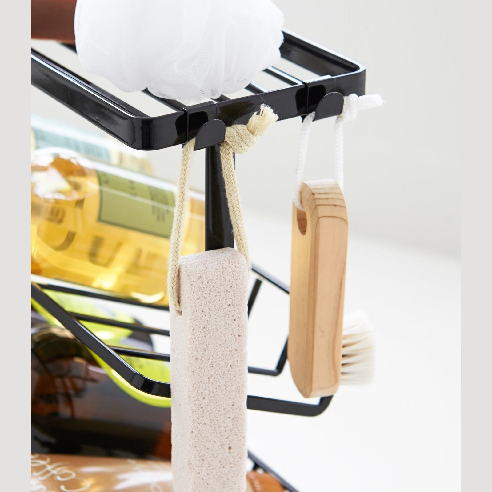 Close up view of black Freestanding Shower Caddy hooks holding beauty items by Yamazaki Home.