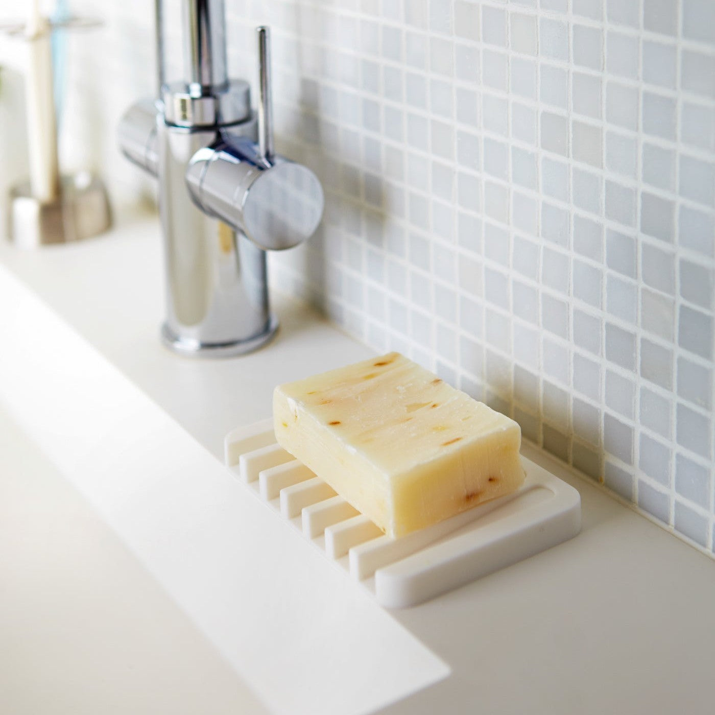 White Self-Draining Soap Tray holding soap on sink counter by Yamazaki Home.