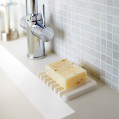 White Self-Draining Soap Tray holding soap on sink counter by Yamazaki Home.