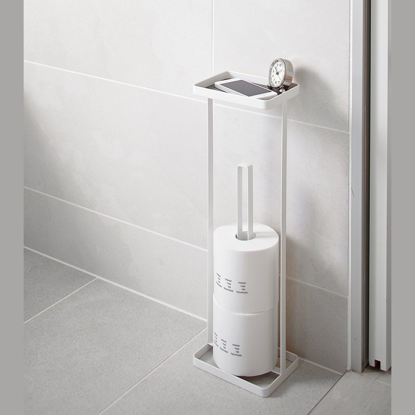 White Toilet Paper Stocker holding phone, clock and toilet paper in bathroom by Yamazaki home.
