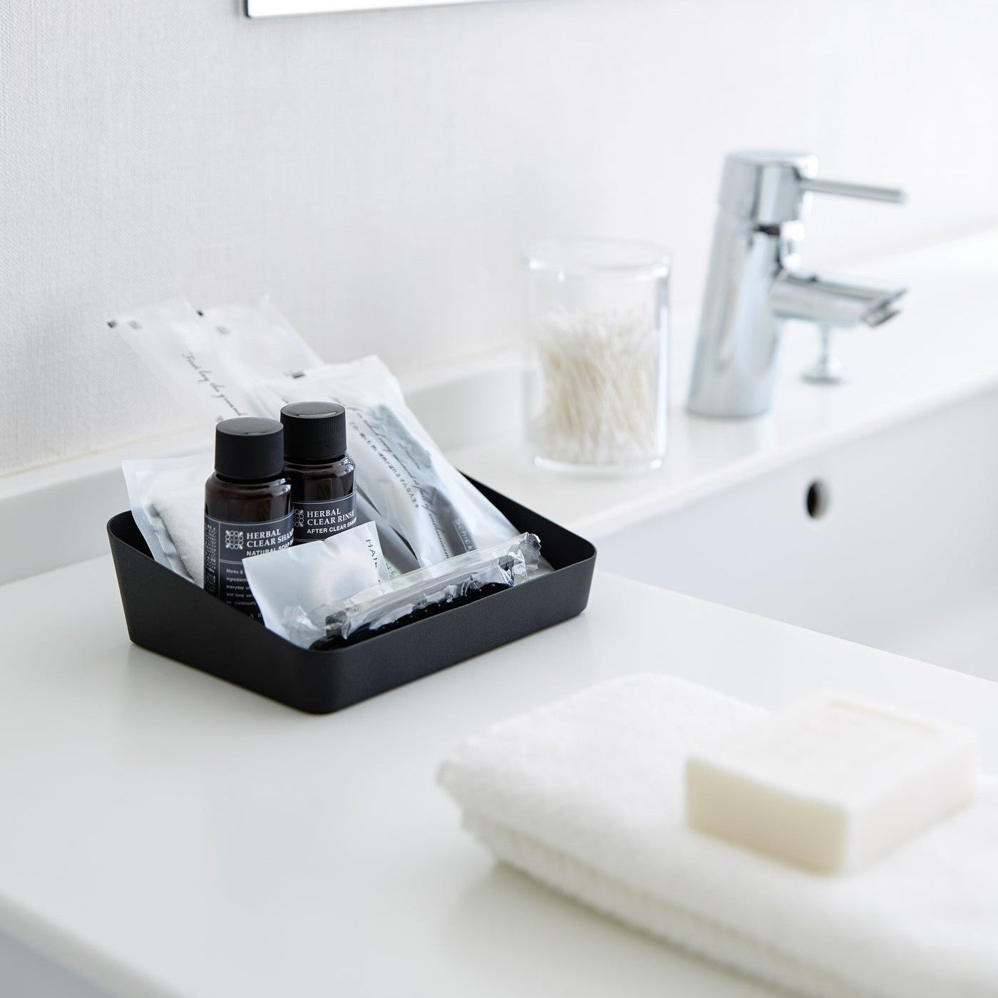 Medium black Accessory Tray holding beauty items on bathroom sink counter by Yamazaki Home.