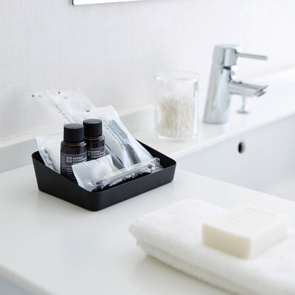 Medium black Accessory Tray holding beauty items on bathroom sink counter by Yamazaki Home.