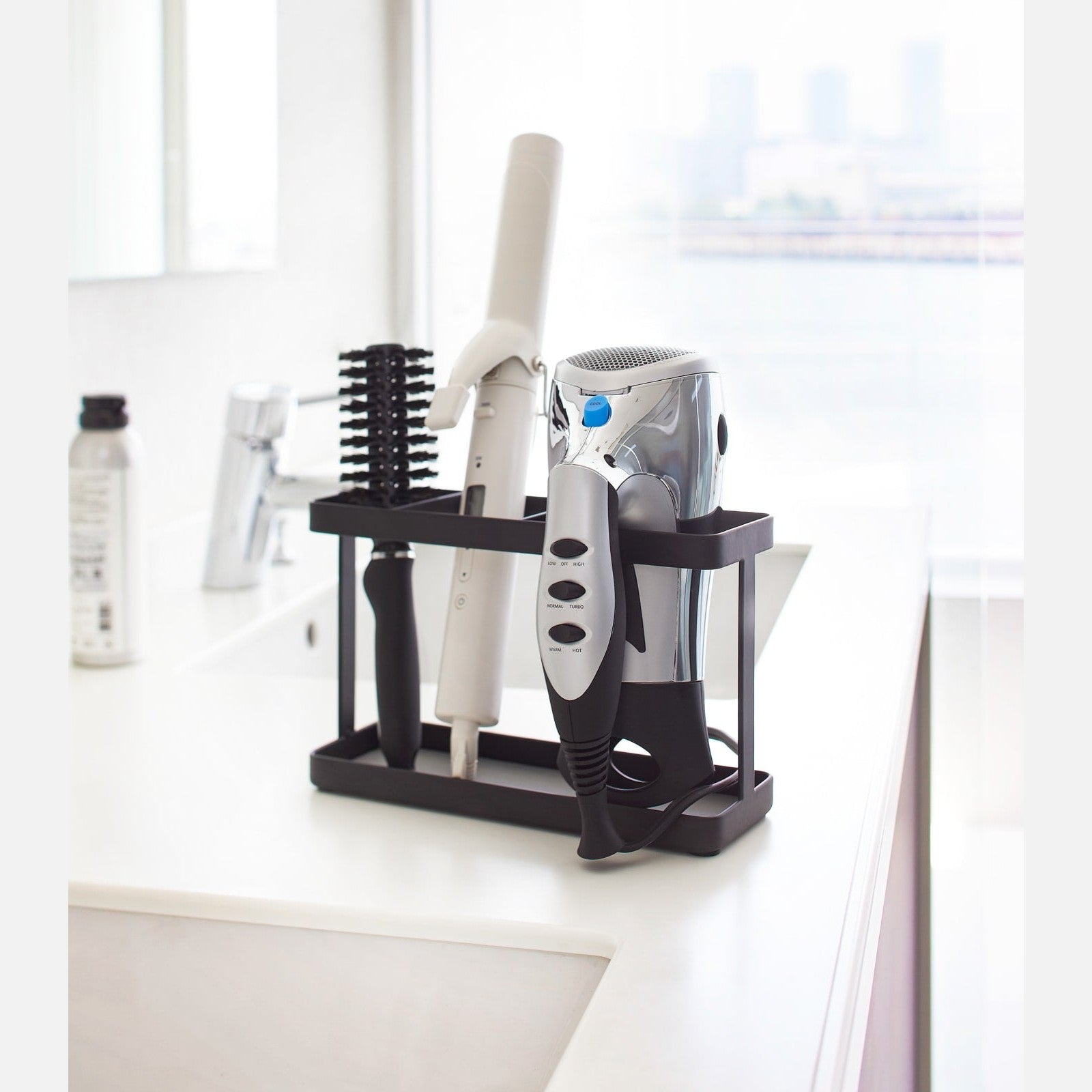 Black Haircare Appliance Holder holding hair tools and brush in bathroom by Yamazaki Home.