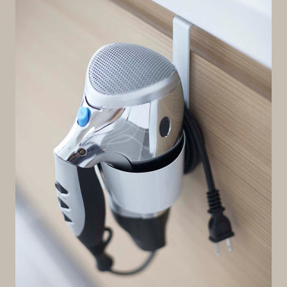 Close up view of white Blow Dryer Holder holding blow dryer on bathroom cabinet by Yamazaki Home.