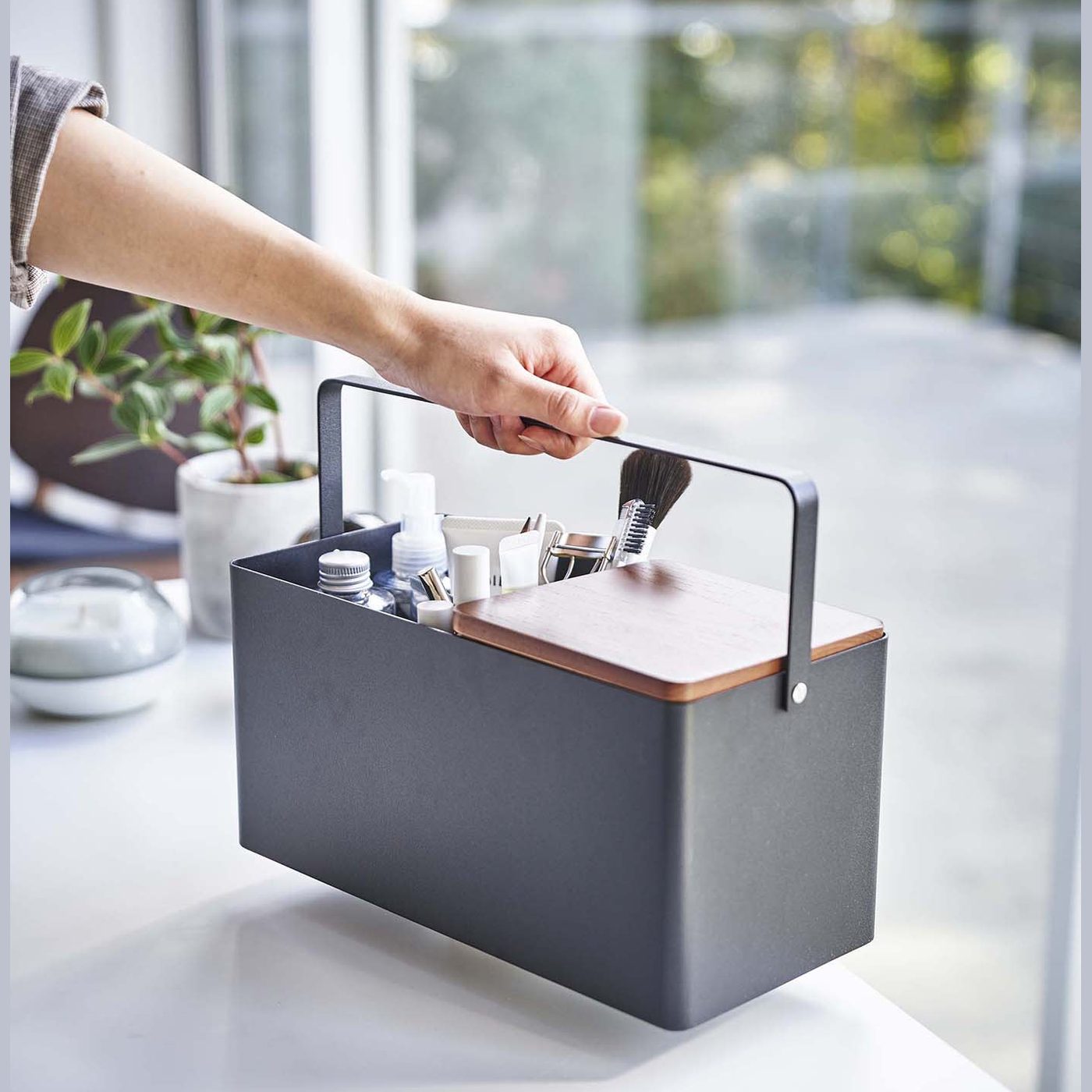 Person holding handle of black Makeup Organizer containing makeup products by Yamazaki Home.
