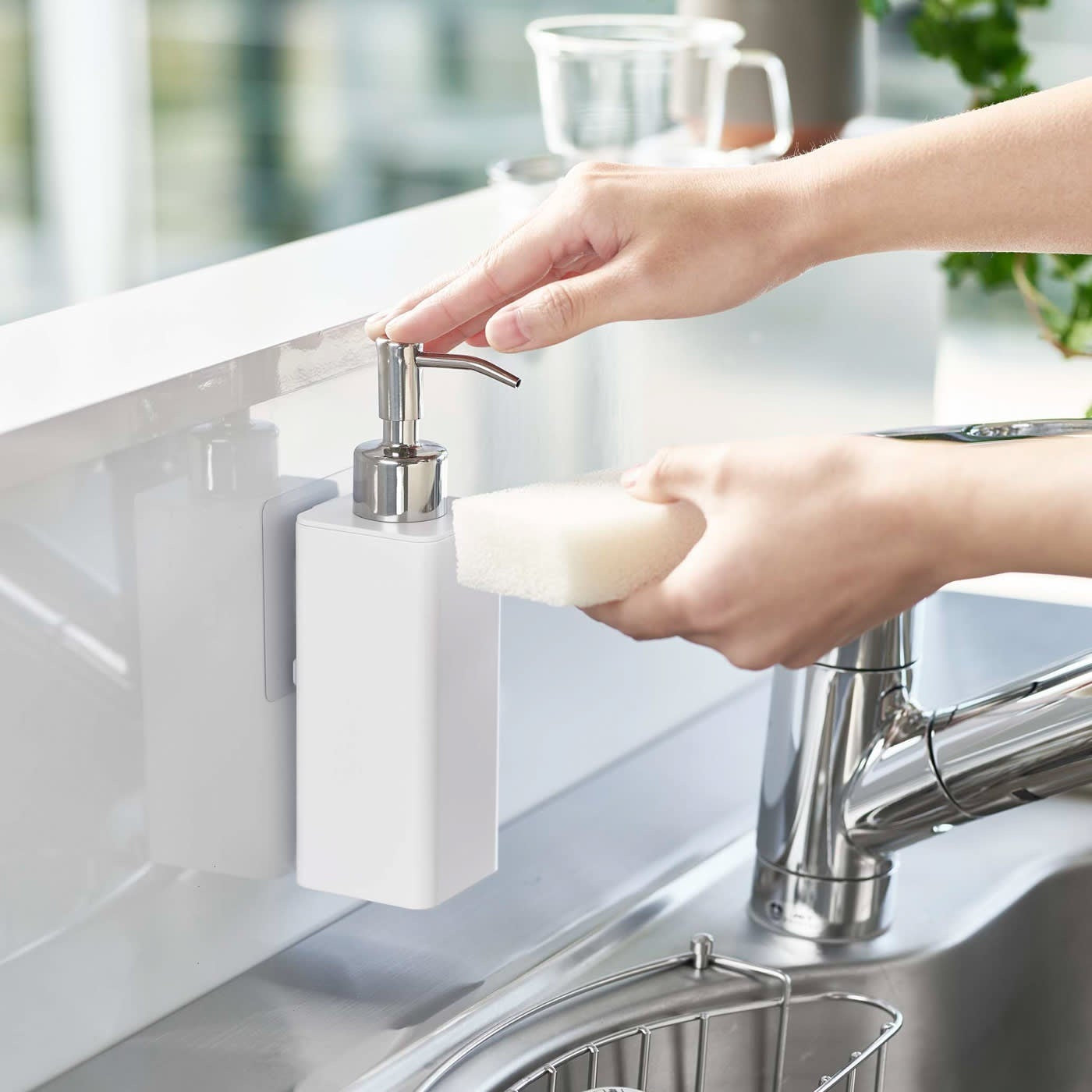 Dispensing soap from white Yamazaki Home square soap dispenser onto dish sponge