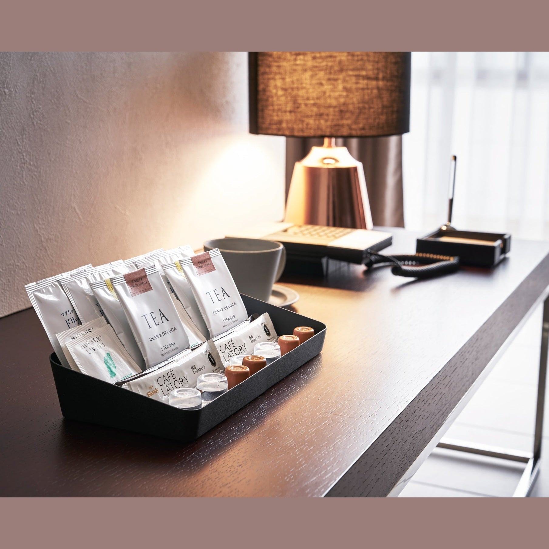 Side view of black Accessory Tray holding tea bags and coffee pods on desk by Yamazaki Home.