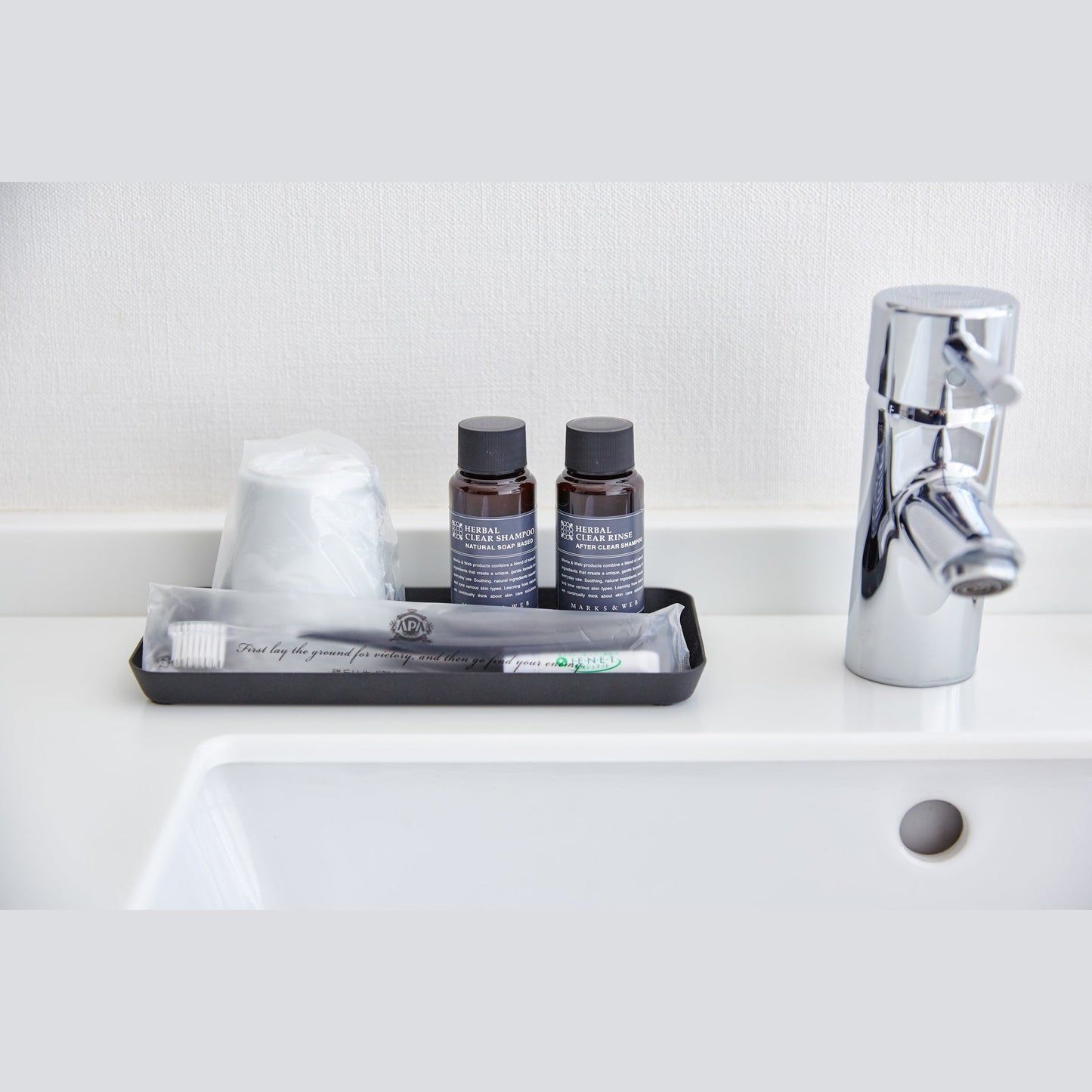 Front view of flat black Accessory Tray holding toothbrush, cup, and soap on bathroom sink counter by Yamazaki Home.