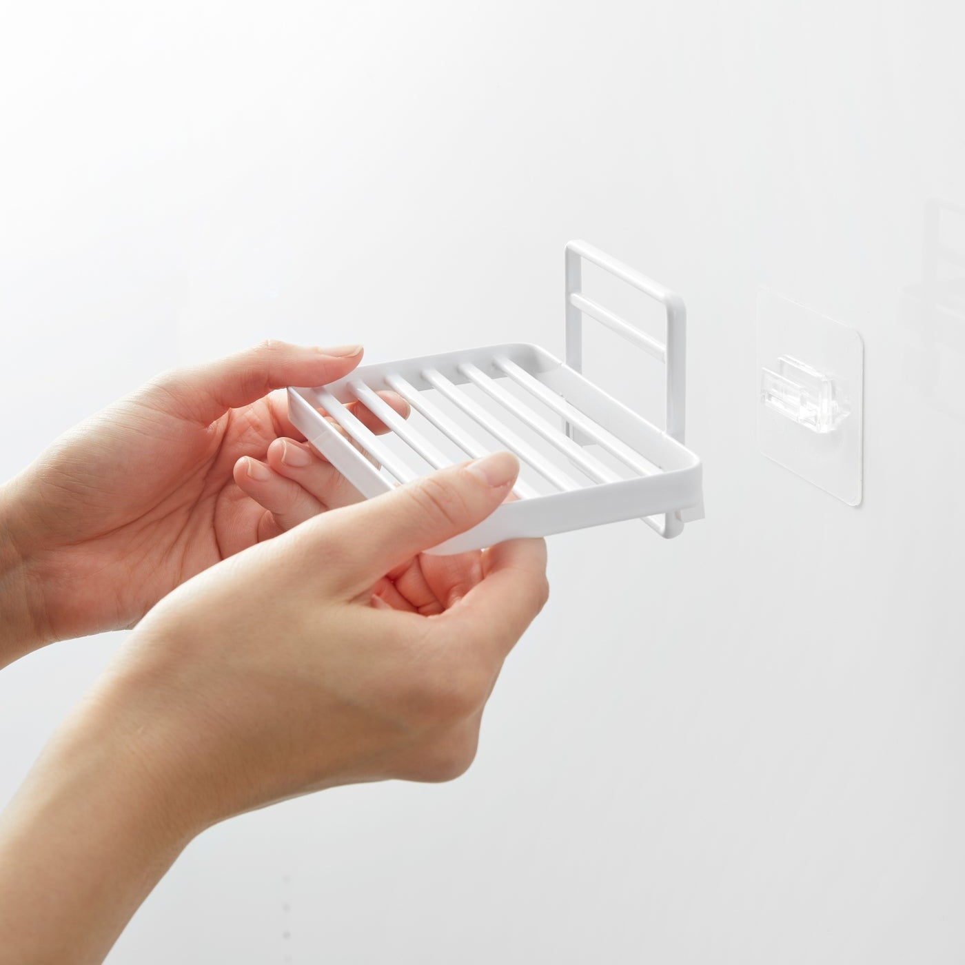 Hands installing Yamazaki Home's white Traceless Adhesive Soap Tray on a bathroom wall, demonstrating its ease of use.