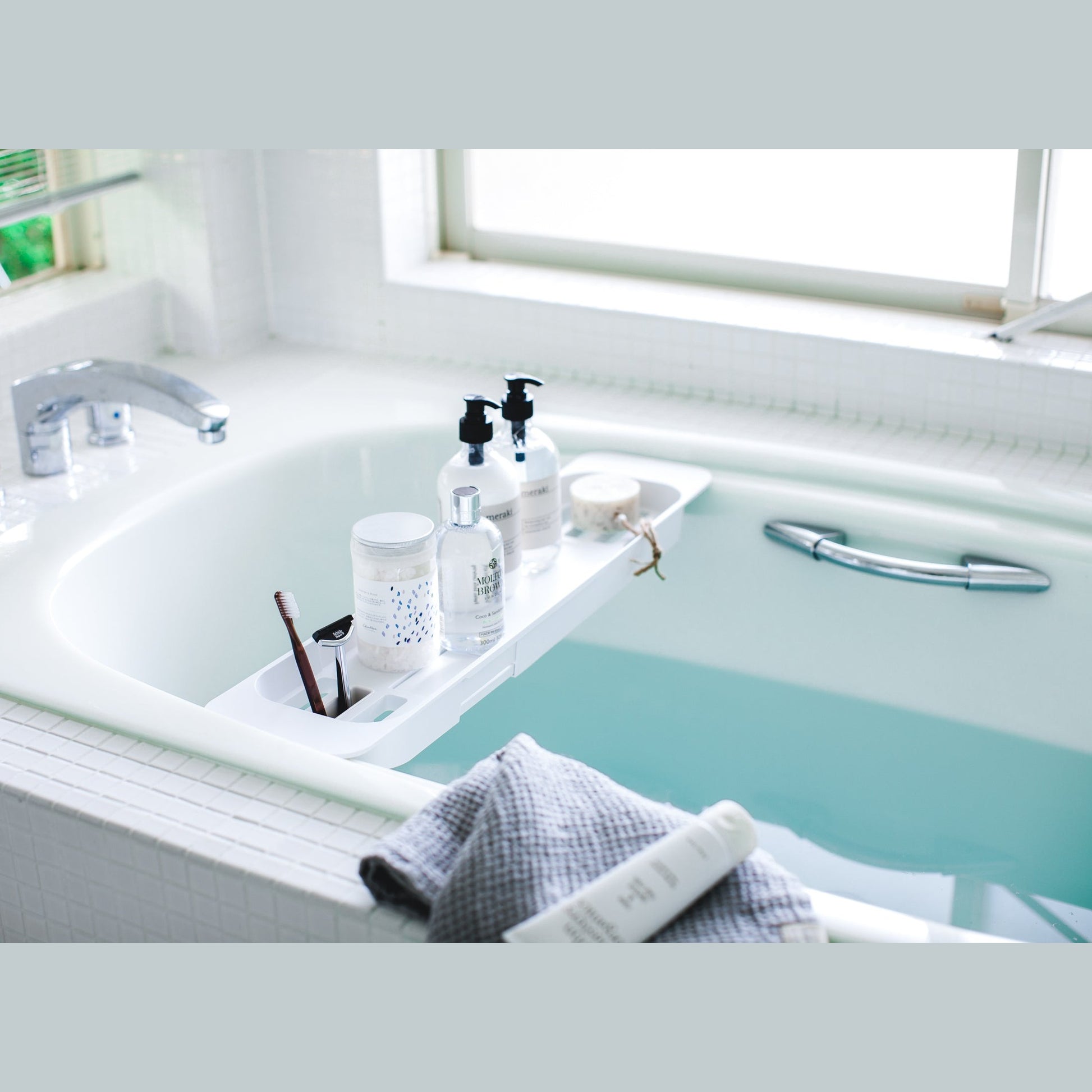 White Expandable Bathtub Caddy holding beauty cleaning products in bathtub by Yamazaki Home.