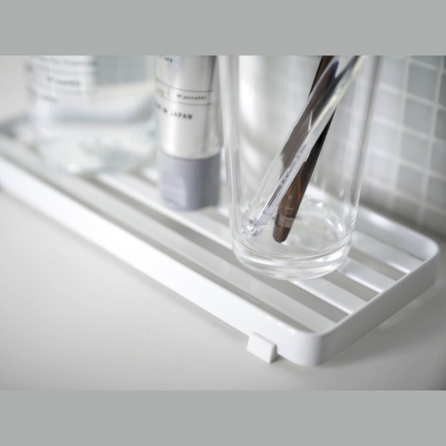 Close up view of white Slotted Tray holding sink accessories in bathroom by Yamazaki Home.