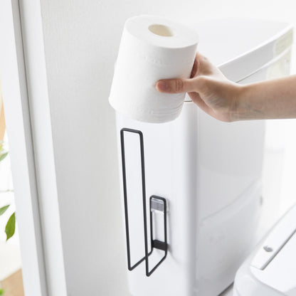 A toilet paper roll being placed on a black Yamazaki Home Traceless Adhesive Toilet Paper Holder