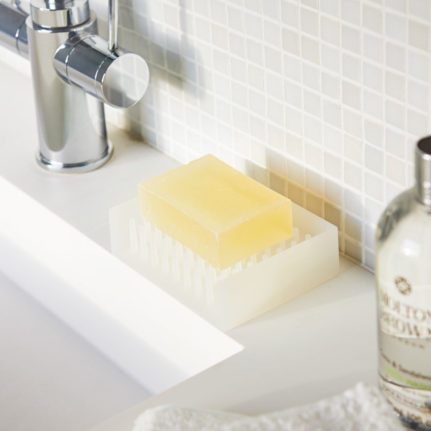 White Self-Draining Soap Dish holding soap bar on sink counter by Yamazaki Home.
