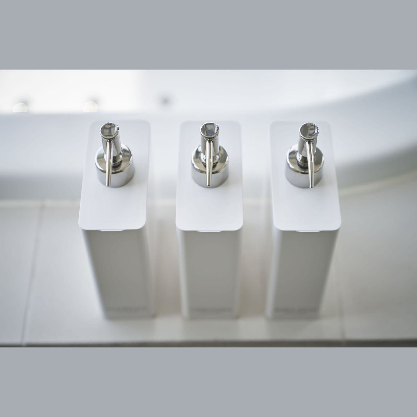 Aerial view of Yamazaki Home white Shampoo, Conditioner, and Body Soap dispensers.