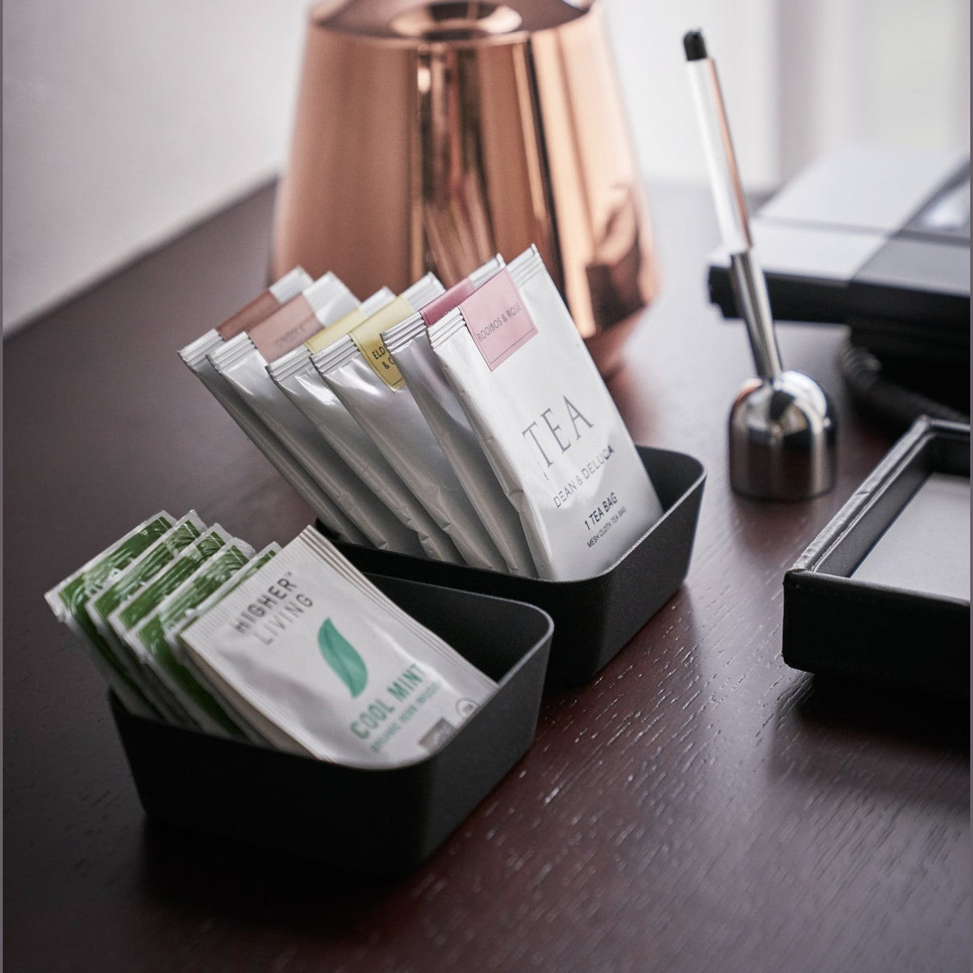 Side view of small black Accessory Trays holding tea bags on office table by Yamazaki Home.