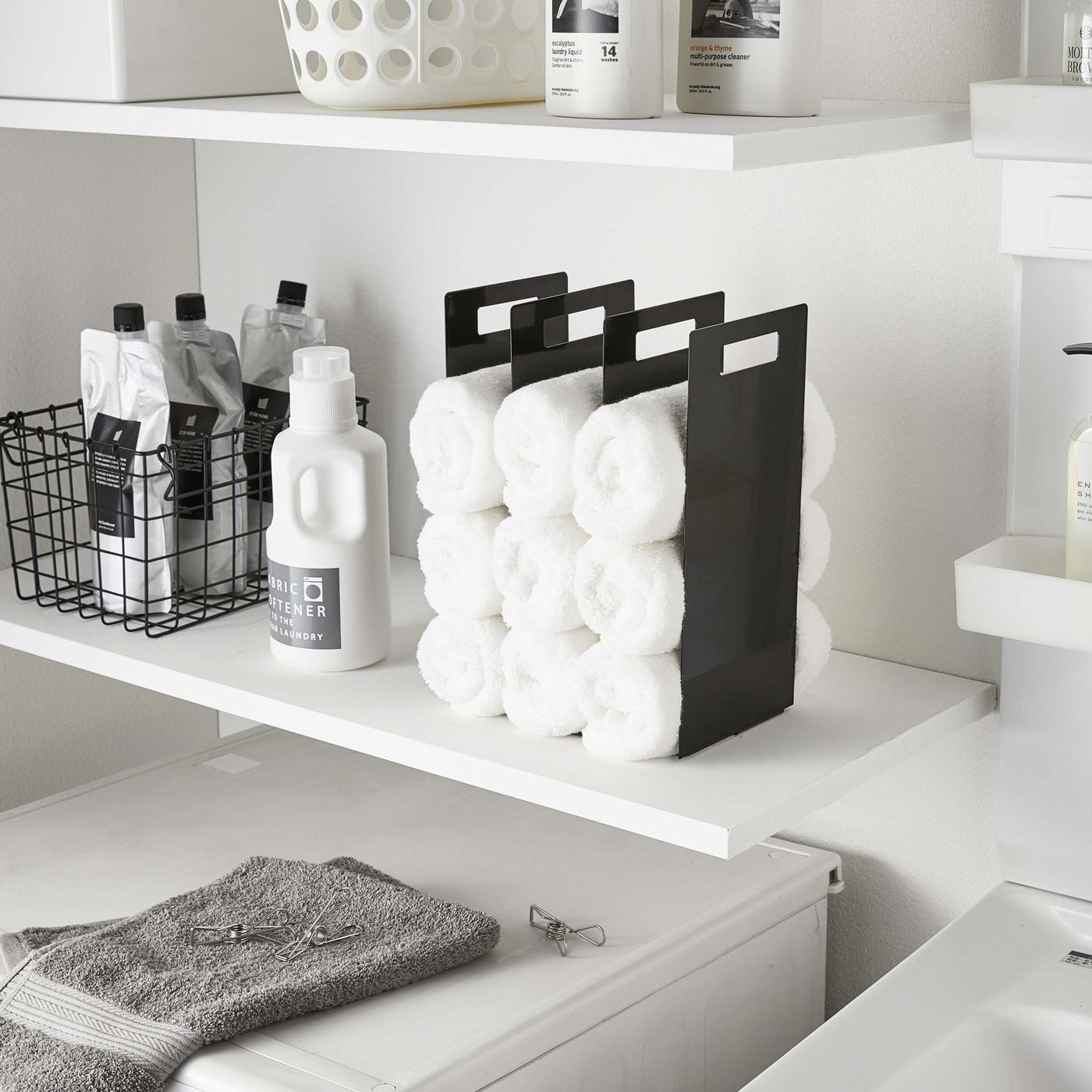 Black Towel Storage Organizer holding towels in laundry room by Yamazaki Home.