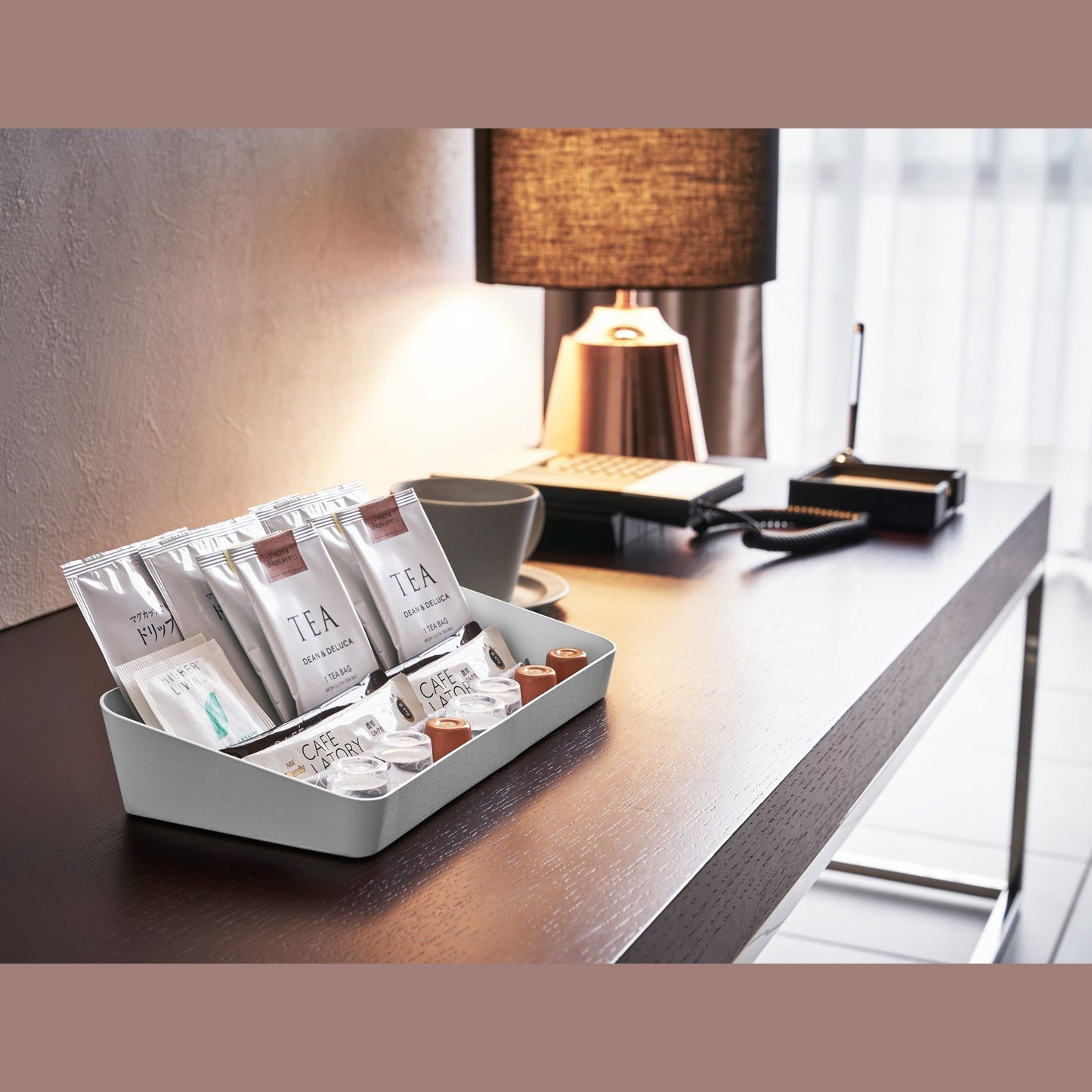 Side view of white Accessory Tray holding tea bags and espresso pods on desk by Yamazaki Home.