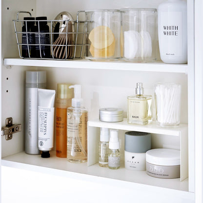 Open medicine cabinet showing white countertop riser on bottom shelf. Upper level of the riser holds perfume and hair products, while skincare and small sprays are stored on the bottom.