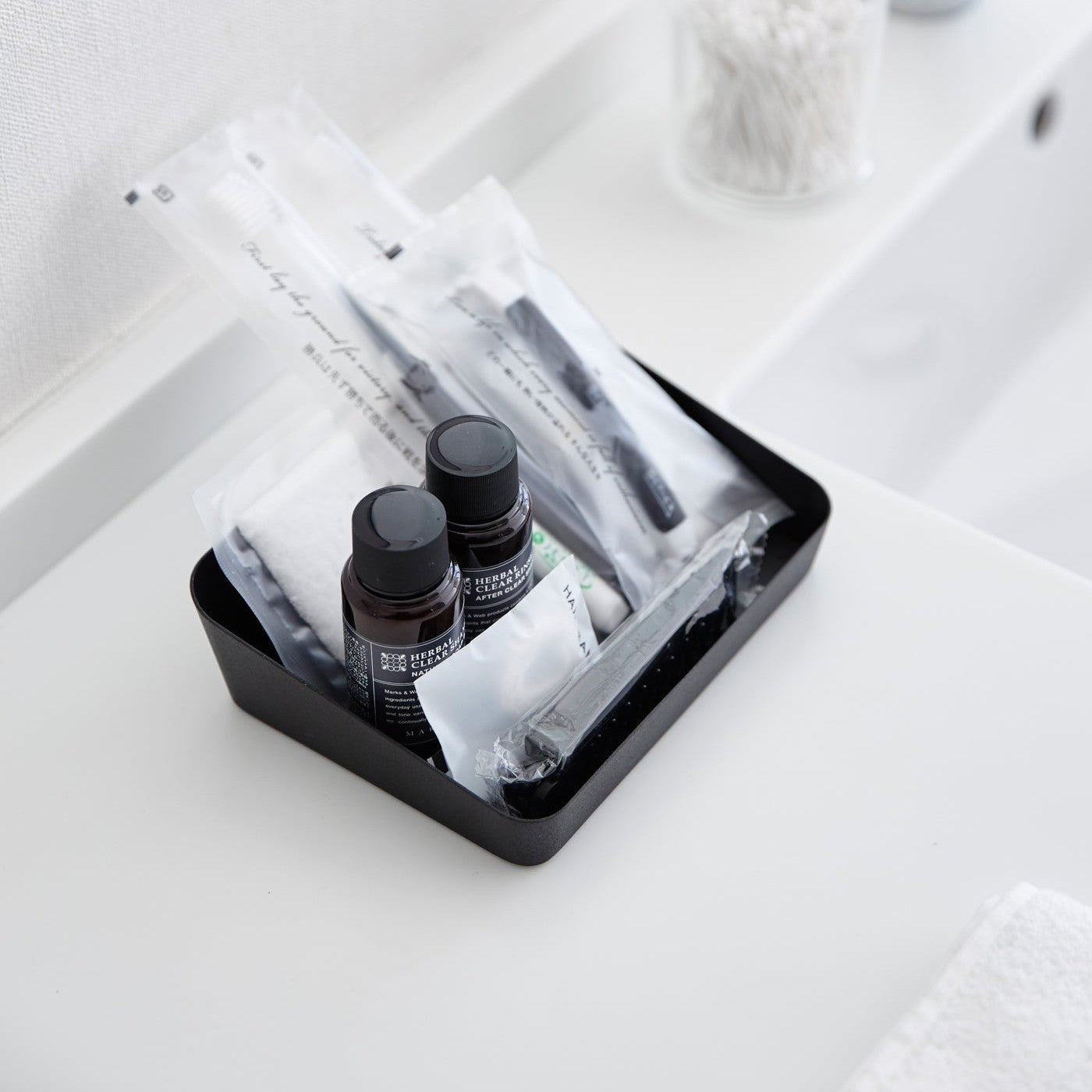 Aerial view of medium black Accessory Tray holding beauty items on bathroom sink counter by Yamazaki Home.