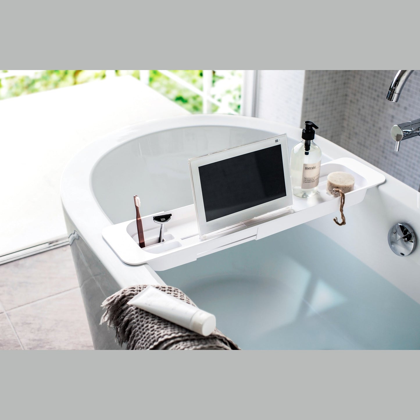 White Expandable Bathtub Caddy holding beauty items and tablet by Yamazaki Home.