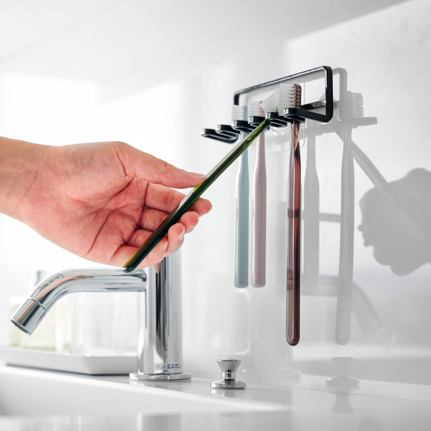 Yamazaki Home's Traceless Adhesive Toothbrush Holder, black, mounted on a bathroom wall with four colorful toothbrushes and a chrome faucet.
