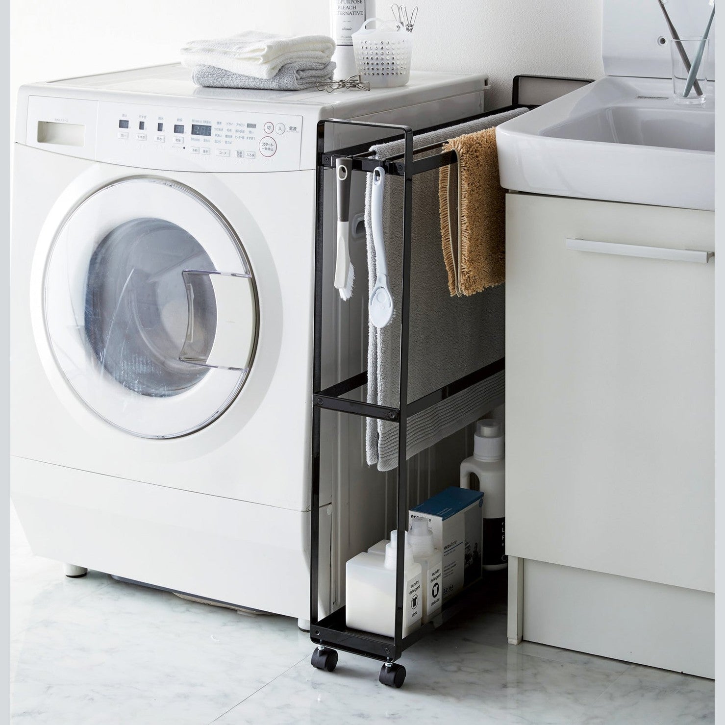 Black Rolling Towel Rack holding bath mats and cleaning products in laundry roomby Yamazaki Home.