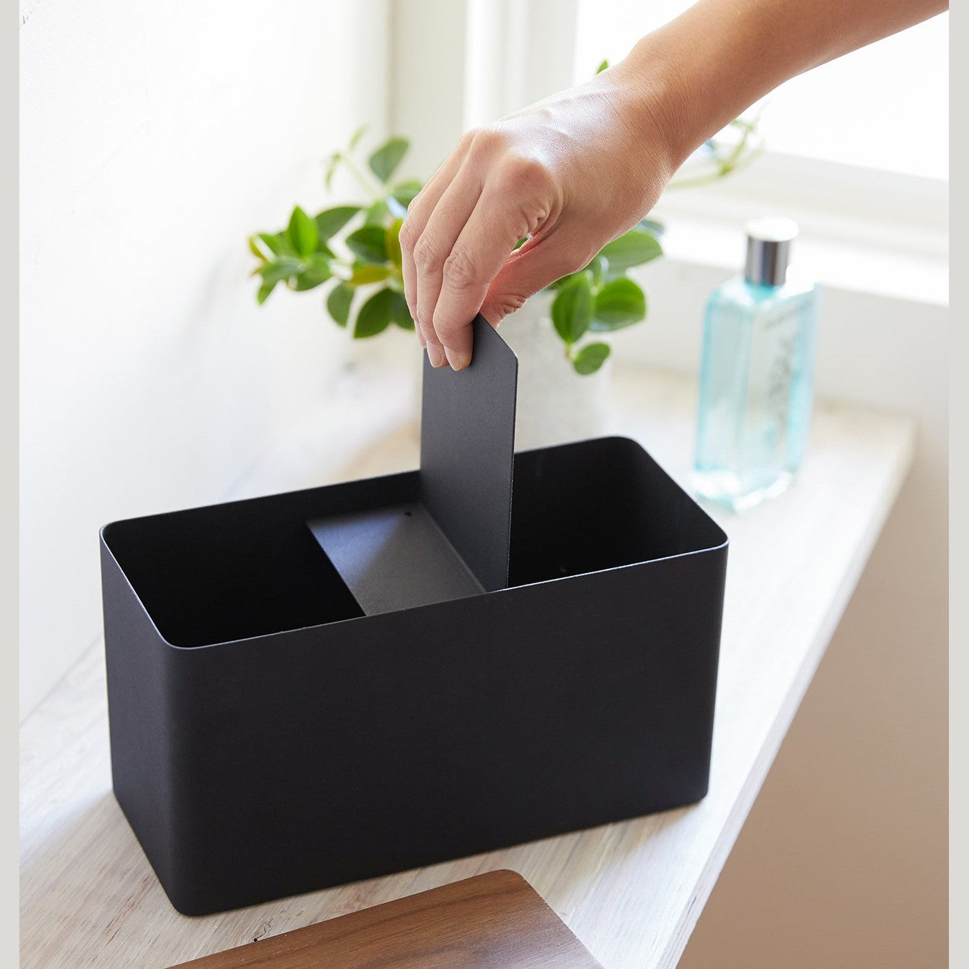 Person inserting divider into black Countertop Organizer with lid off by Yamazaki Home.